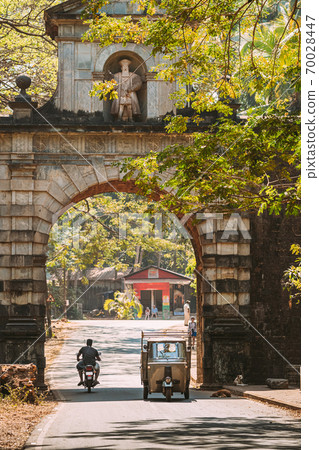 Old Goa, India. Auto Rickshaw Or Tuk-tuk Moving Through The Old Viceroy s Arch. Famous Vasco Da Gama Gate Landmark And Historical Heritage.Street In Sunny Day Old Goa, India. Auto Rickshaw Or Tuk-tuk Moving Through The Old Viceroy s Arch. Famous Vasco Da Gama Gate Landmark And Historical Heritage.Street In Sunny Day 70028447