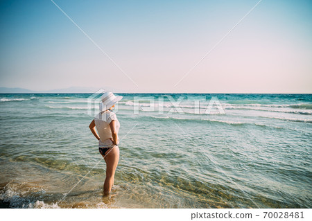 Young Caucasian Lady Woman In Swimsuit And Summer Hat Standing In Sea. Vacation On Sea Ocean Beach Young Caucasian Lady Woman In Swimsuit And Summer Hat Standing In Sea. Vacation On Sea Ocean Beach 70028481