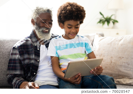 Senior man and grandson using digital tablet on couch at home 70028547