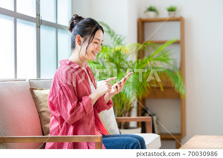 一個女人在沙發上放鬆的同時操作智能手機。 70030986