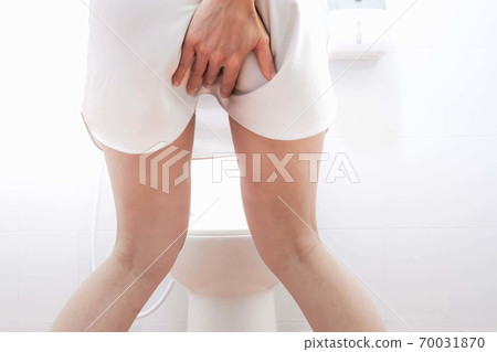 Women wearing white sleepwear, Sitting on the toilet Hand holding the stomach,standing in the toilet, Holding a toilet paper, bent, stomachache health care concept 70031870