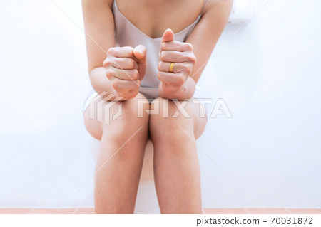 Women wearing white sleepwear, Sitting on the toilet Hand holding the stomach,standing in the toilet, Holding a toilet paper, bent, stomachache health care concept 70031872
