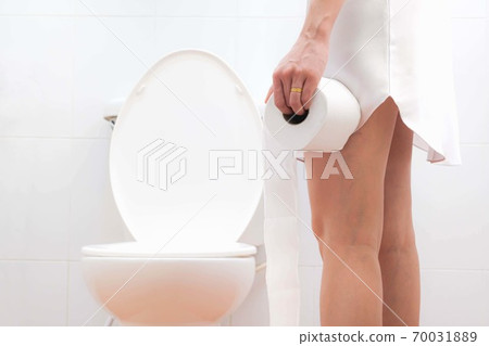 Women wearing white sleepwear, Sitting on the toilet Hand holding the stomach,standing in the toilet, Holding a toilet paper, bent, stomachache health care concept 70031889