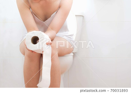 Women wearing white sleepwear, Sitting on the toilet Hand holding the stomach,standing in the toilet, Holding a toilet paper, bent, stomachache health care concept 70031893