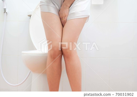 Women wearing white sleepwear, Sitting on the toilet Hand holding the stomach,standing in the toilet, Holding a toilet paper, bent, stomachache health care concept 70031902
