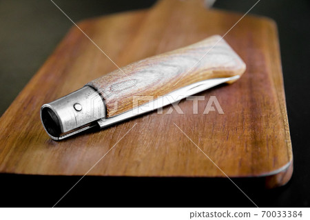 Wooden cutting board and pocket knife on a black table Wooden cutting board and pocket knife on a black table 70033384