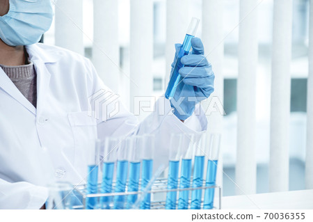Scientists hold a glass tube filled with blue chemical liquid for research and analysis in a laboratory 70036355