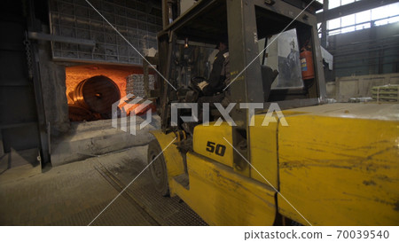 Camera is moving forward of Loader loads aluminum ingots into a blast furnace. Aluminium foundry furnace loaded with metal. Red hot flames glowing and liquid melting. 70039540