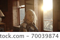 portrait of a beautiful old Granny in a cozy wooden room against the background of sunset or sunrise. 70039874