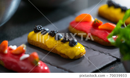Decorating pink glaze eclair with strawberry, mint. Modern desserts and cakes. Cupcakes with cream filling. Professional pastry. Decorating pink glaze eclair with strawberry, mint. Modern desserts and cakes. Cupcakes with cream filling. Professional pastry. 70039933