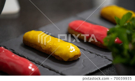Yellow and pink glaze eclair on stone plates. Modern desserts and cakes. Cupcakes with cream filling. Professional pastry. Yellow and pink glaze eclair on stone plates. Modern desserts and cakes. Cupcakes with cream filling. Professional pastry. 70039935