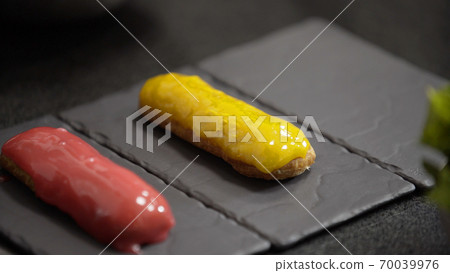 Yellow and pink glaze eclair on stone plates. Modern desserts and cakes. Cupcakes with cream filling. Professional pastry. Yellow and pink glaze eclair on stone plates. Modern desserts and cakes. Cupcakes with cream filling. Professional pastry. 70039976