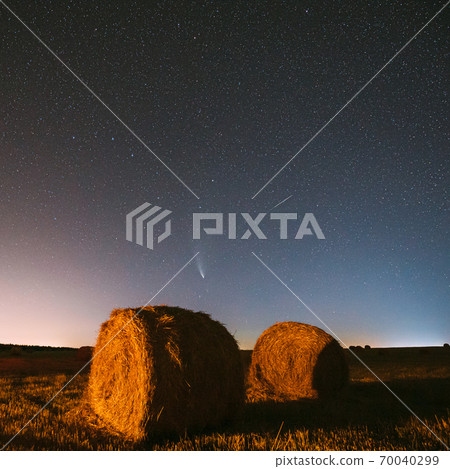 Meteor And Comet Neowise C2020 F3 In Night Starry Sky Above Haystacks In Summer Agricultural Field. Night Stars Above Rural Landscape With Hay Bales After Harvest 70040299