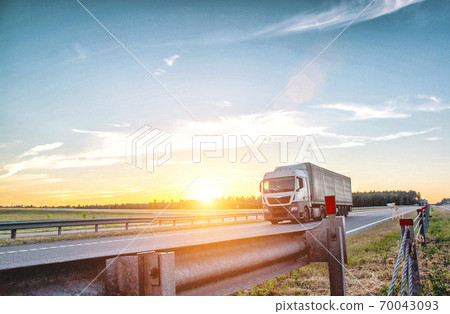 A tilt euro truck carries cargo along the highway in the evening against the backdrop of sunset. Bump stop on the road, safety, international transportation 70043093