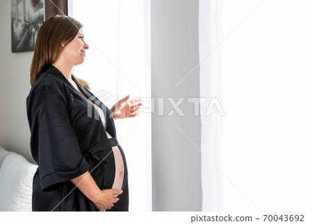 Young pregnant woman watching out from the window, pregnancy concept 70043692
