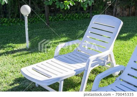 White plastic sun loungers for sunbathing in the garden near a swimming pool 70045335