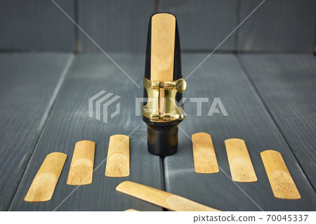 Replacement reeds and saxophone mouthpiece with clamp and golden adjustment screws on gray wooden table 70045337