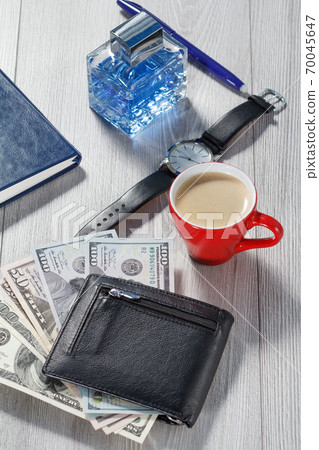 Man perfume, pen, watch with a black leather strap, cup of coffee, notebook and black leather wallet with dollar bills Man perfume, pen, watch with a black leather strap, cup of coffee, notebook and black leather wallet with dollar bills 70045647