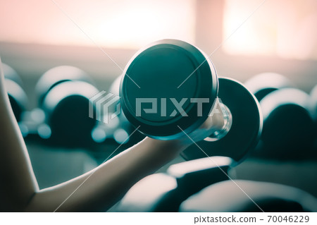 Woman arm lifting black sport dumbell showing strength in an indoor fitness gym for healthy lifestyle concept. Woman arm lifting black sport dumbell showing strength in an indoor fitness gym for healthy lifestyle concept. 70046229