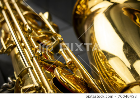 Keys, rods and bell of a golden and shiny saxophone, in the foreground, on gray wooden background Keys, rods and bell of a golden and shiny saxophone, in the foreground, on gray wooden background 70046458