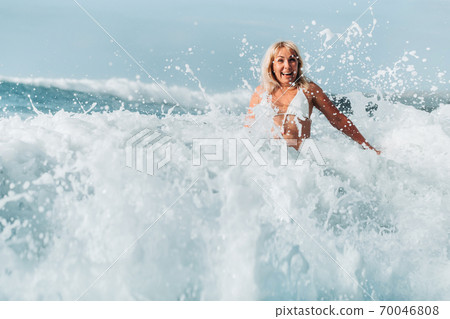 A girl with wet hair jumps over large waves in the Atlantic ocean, around a wave with splashes of spray and water drops.Tenerife.Spain 70046808