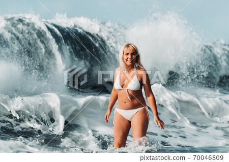A girl with wet hair jumps over large waves in the Atlantic ocean, around a wave with splashes of spray and water drops.Tenerife.Spain 70046809