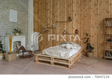 Wooden bedroom with a white fireplace. Wall with wooden panels and bricks. Near the fireplace a wooden horse. High quality photo 70047219