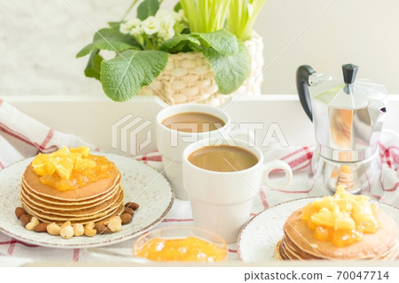 Perfect breakfast for 2. Tray with pancakes with orange jam and nuts on vintage plates and 2 white coffee cups 70047714