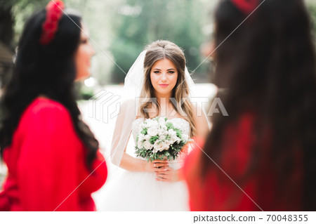 Beautiful bride in elegant white dress holding bouquet posing in park 70048355