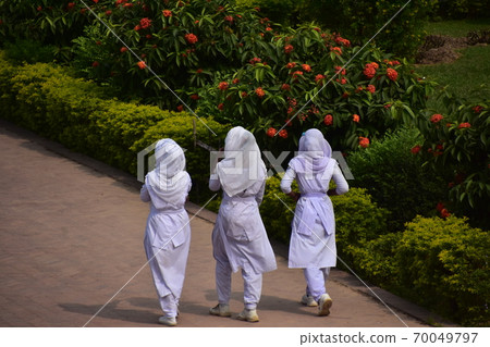 A Muslim schoolgirl walking along the sidewalk of the unfinished castle ruins of Lalbagh Fort Gardens in Dhaka, Bangladesh 70049797