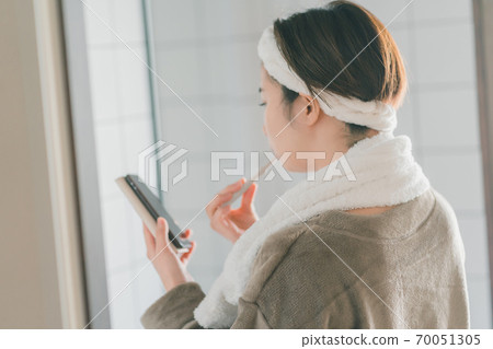 A woman brushing teeth while looking at a smartphone 70051305