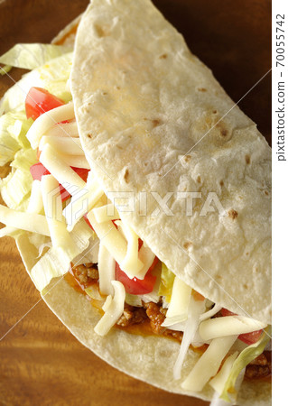 Tacos with cheese, cherry tomatoes and minced meat placed on a round wooden plate 70055742