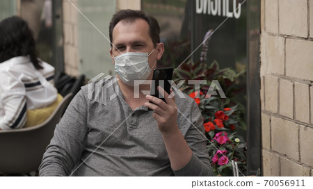 Man in a medical mask talking on a mobile phone using a modern messenger for video communication Man in a medical mask talking on a mobile phone using a modern messenger for video communication 70056911