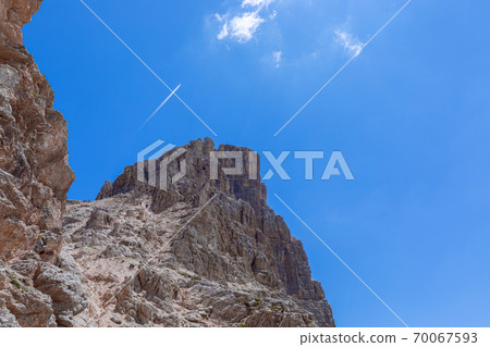 Climbers and hikkers climb to the top of the Sassongher mountain against the blue sky Climbers and hikkers climb to the top of the Sassongher mountain against the blue sky 70067593