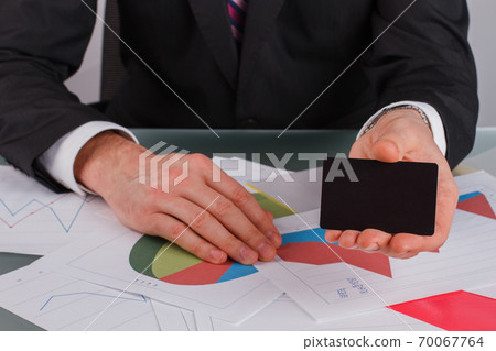 Businessman or financier giving a business card while sitting at the table. Businessman or financier giving a business card while sitting at the table. 70067764