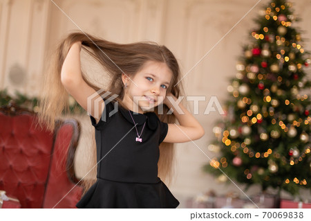 A little girl opens a Christmas present from Santa. Christmas tale. Happy childhood A little girl opens a Christmas present from Santa. Christmas tale. Happy childhood 70069838
