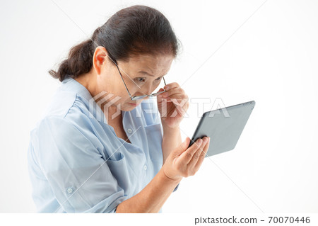 Senior woman looking at a tablet PC with reading glasses Senior woman looking at a tablet PC with reading glasses 70070446