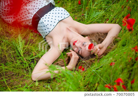 A young long-haired girl enjoys the colors of nature on a blooming poppy field on a hot summer day 70070805