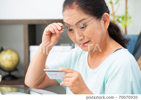 Senior woman looking at a card with reading glasses 70070930
