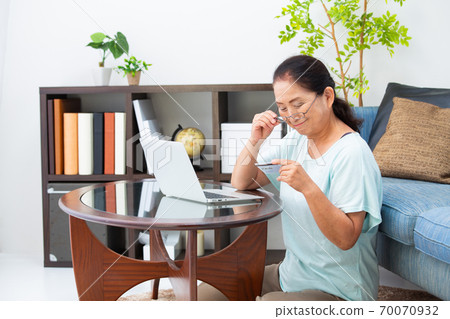 Senior woman looking at a card with reading glasses Senior woman looking at a card with reading glasses 70070932