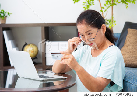 Senior woman looking at a card with reading glasses Senior woman looking at a card with reading glasses 70070933