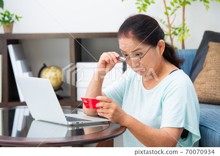 Senior woman looking at a card with reading glasses Senior woman looking at a card with reading glasses 70070934