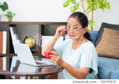 Senior woman looking at a card with reading glasses 70070935