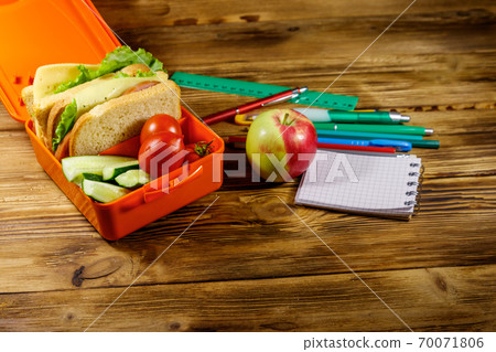 Back to school concept. School supplies, apple and lunch box with sandwiches and fresh vegetables on a wooden desk Back to school concept. School supplies, apple and lunch box with sandwiches and fresh vegetables on a wooden desk 70071806