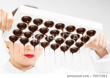 chocolatier pouring excess melted dark chocolate from molds preparing candy 70072962