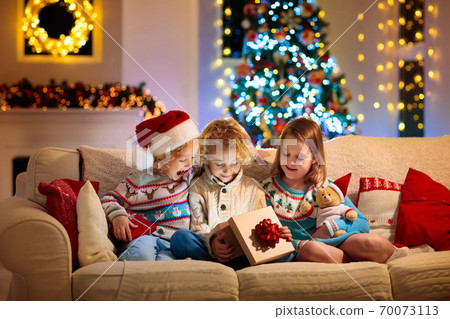 Child at Christmas tree. Kids at fireplace on Xmas Child at Christmas tree. Kids at fireplace on Xmas 70073113