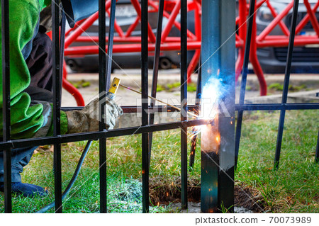 A welder works with metal, welds a metal fence at a construction site, enclosing a site. 70073989