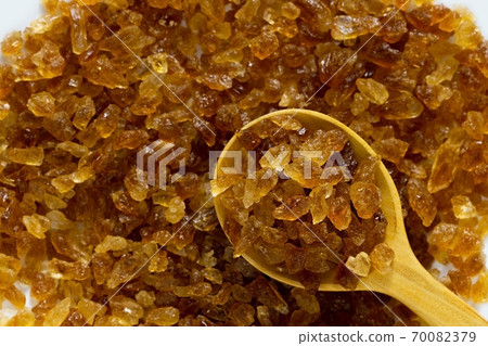 Natural organic brown crystal rock sugar in wooden spoon over brown rock sugar stack. 70082379