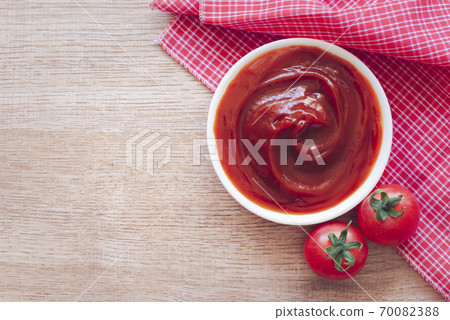Tomato ketchup sauce in ceramic bowl on placemat with tomatoes over wooden background. 70082388