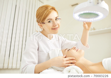 A cosmetologist makes a face mask to a patient 70083226